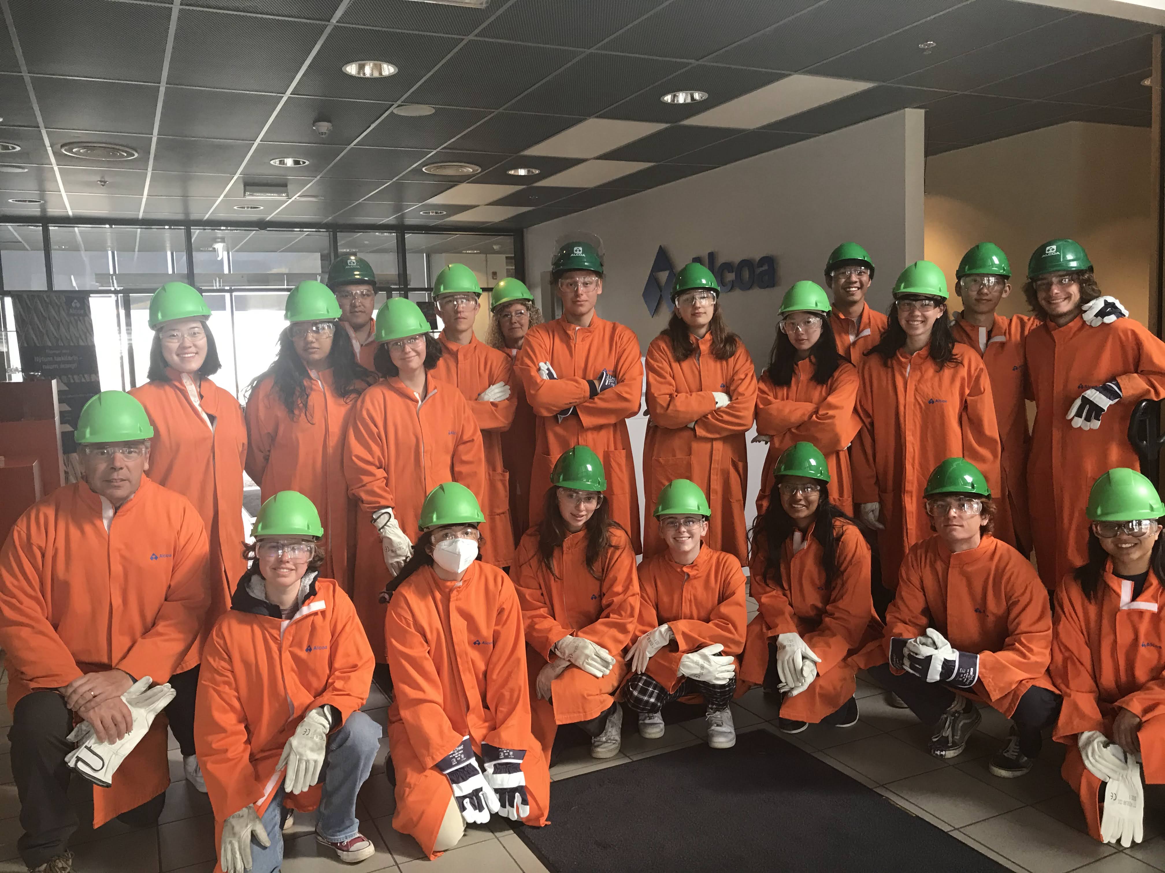 Many students in orange protective suits and green hard hats