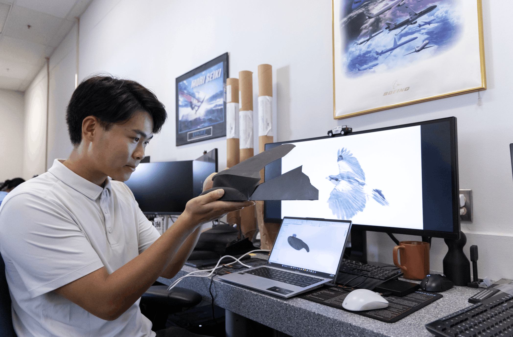 Zhu examining a 3D model of a hawk wing at a desk with dual monitors showing CAD renderings