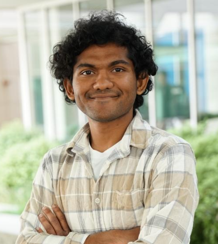 Smiling Mitra plaid shirt, smiling with arms crossed outdoors.