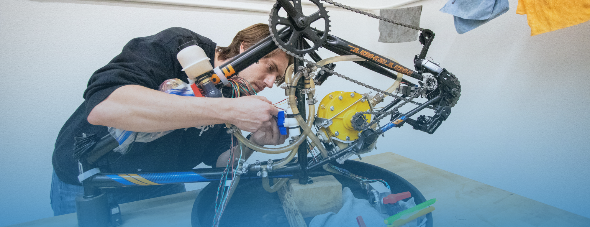 A student attaching wires, tubes, and mechanical parts to a bike frame