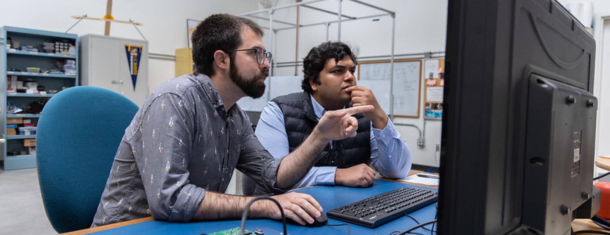 UC Davis graduate students Adam Zufall and Ayush Patnaik sit at a desk working on a payload