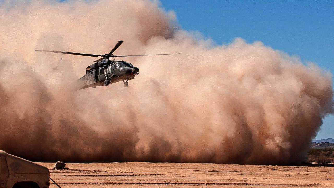 Helicopter emerges from a dust cloud against a blue sky