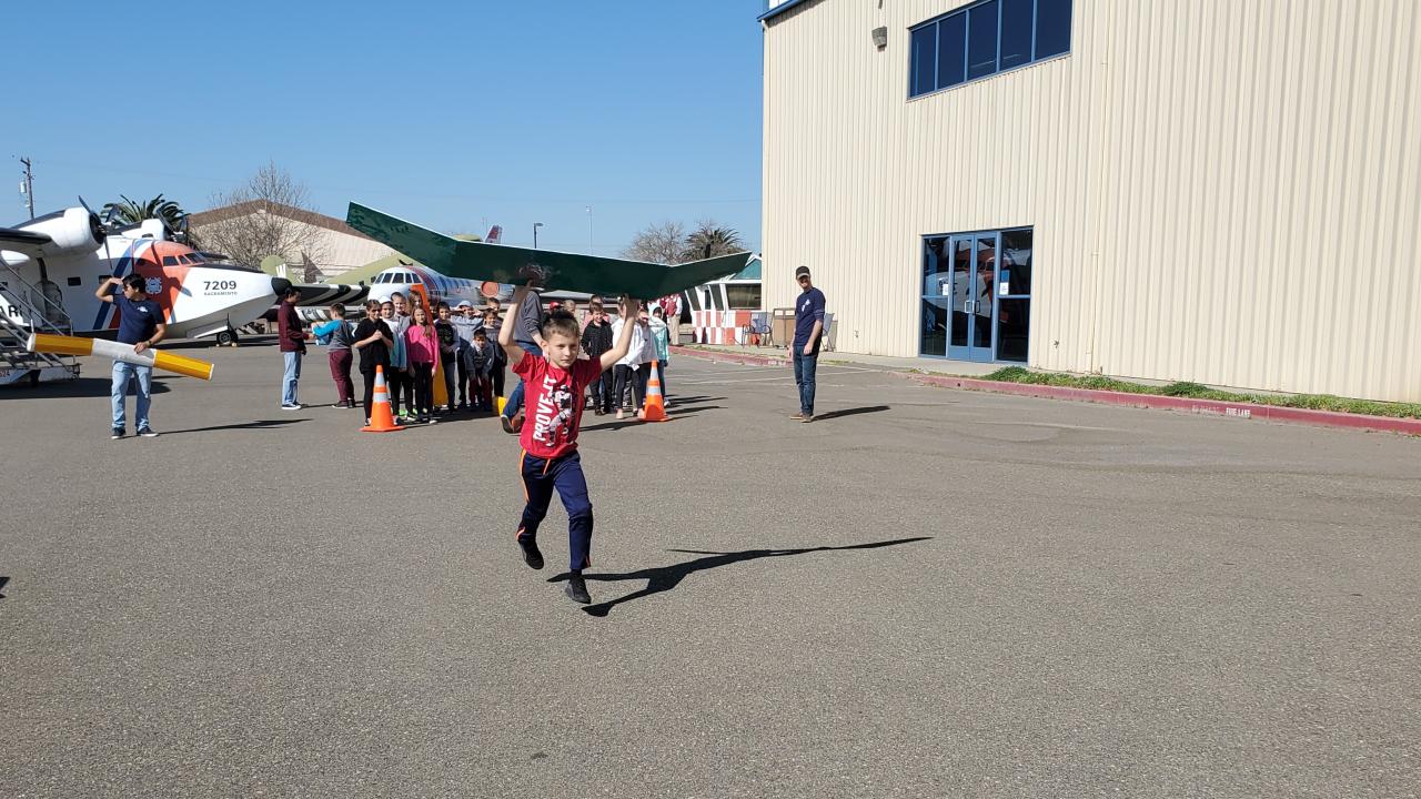 Young student holding makeshift airplane wing and running