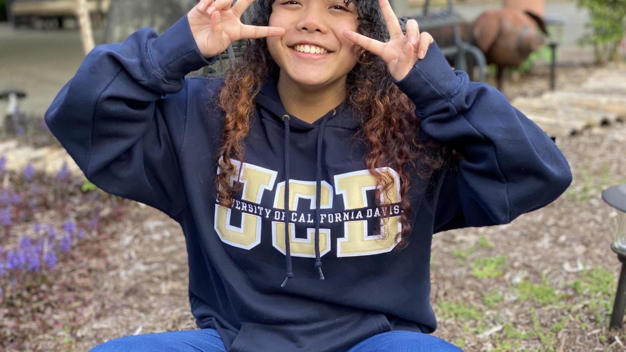 Tichada Tantasirikorn holding up peace signs wearing a UCD sweater