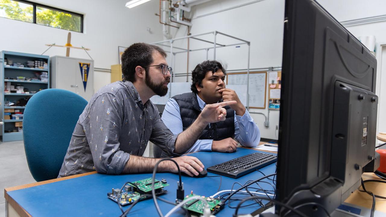 UC Davis graduate students Adam Zufall and Ayush Patnaik sit at a desk working on a payload