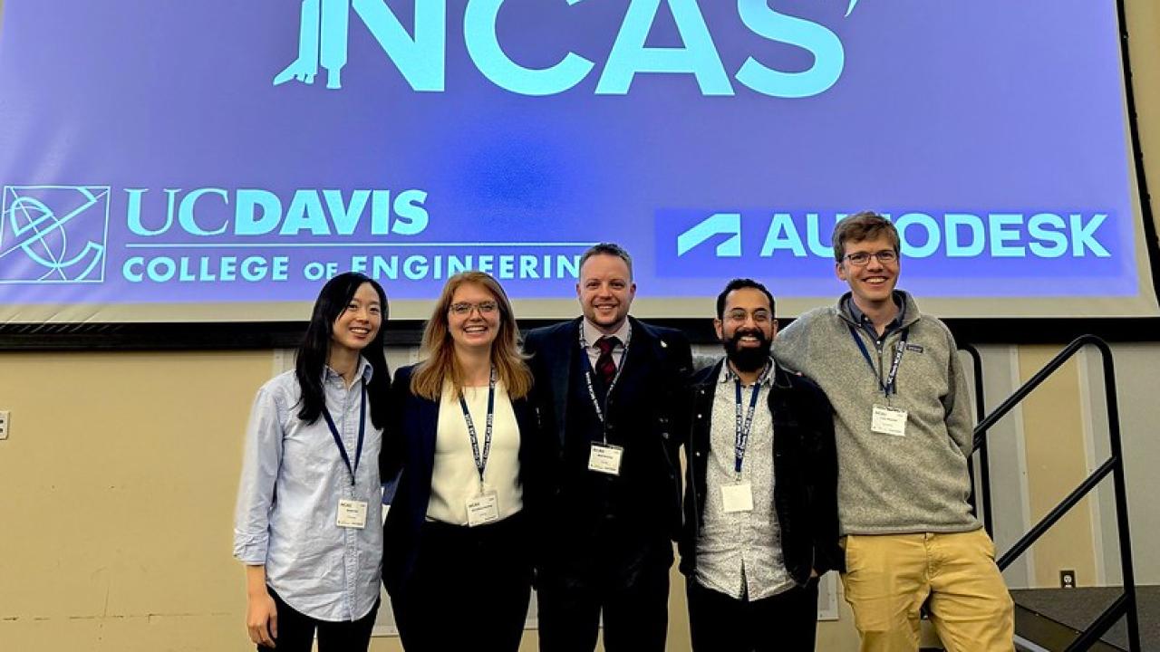 Five people standing under a blue projection screen with the NCAS logo