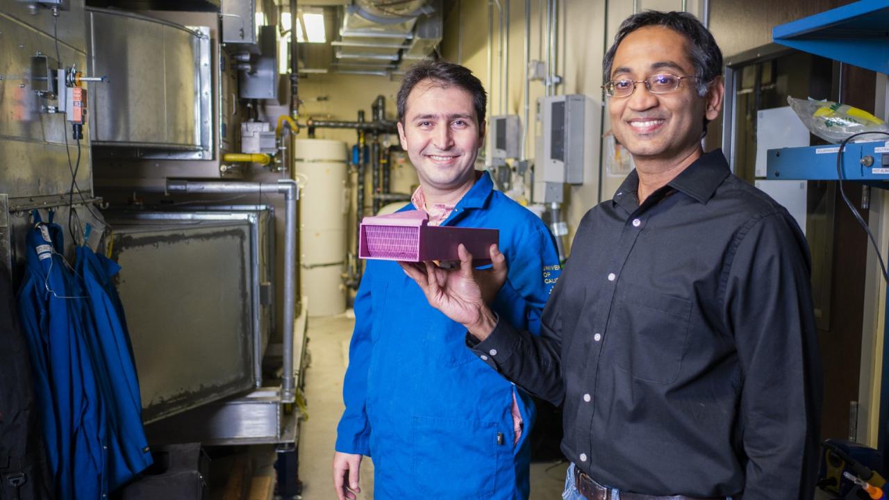 Two researchers hold a pink item while standing in front of large tanks in a laboratory