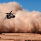 Helicopter emerges from a dust cloud against a blue sky