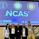Five people standing under a blue projection screen with the NCAS logo