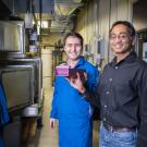 Two researchers hold a pink item while standing in front of large tanks in a laboratory