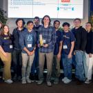 A team of students with a trophy on a stage